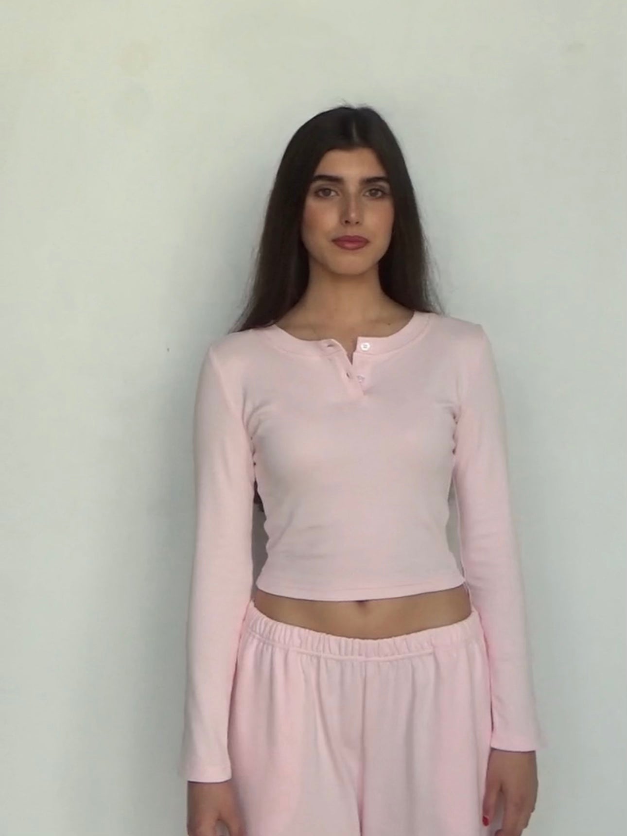 Woman wearing a pink long-sleeve top and pink pants against a plain background