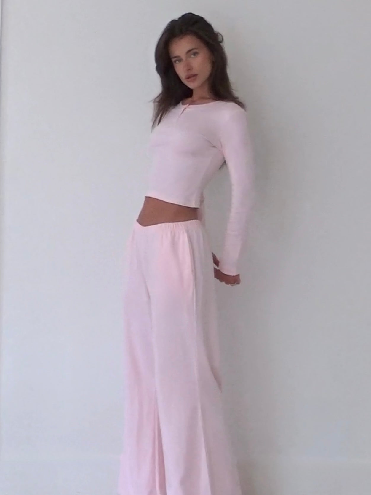 Woman wearing a light pink organic cotton long-sleeve top and organic cotton wide-leg pants against a white background