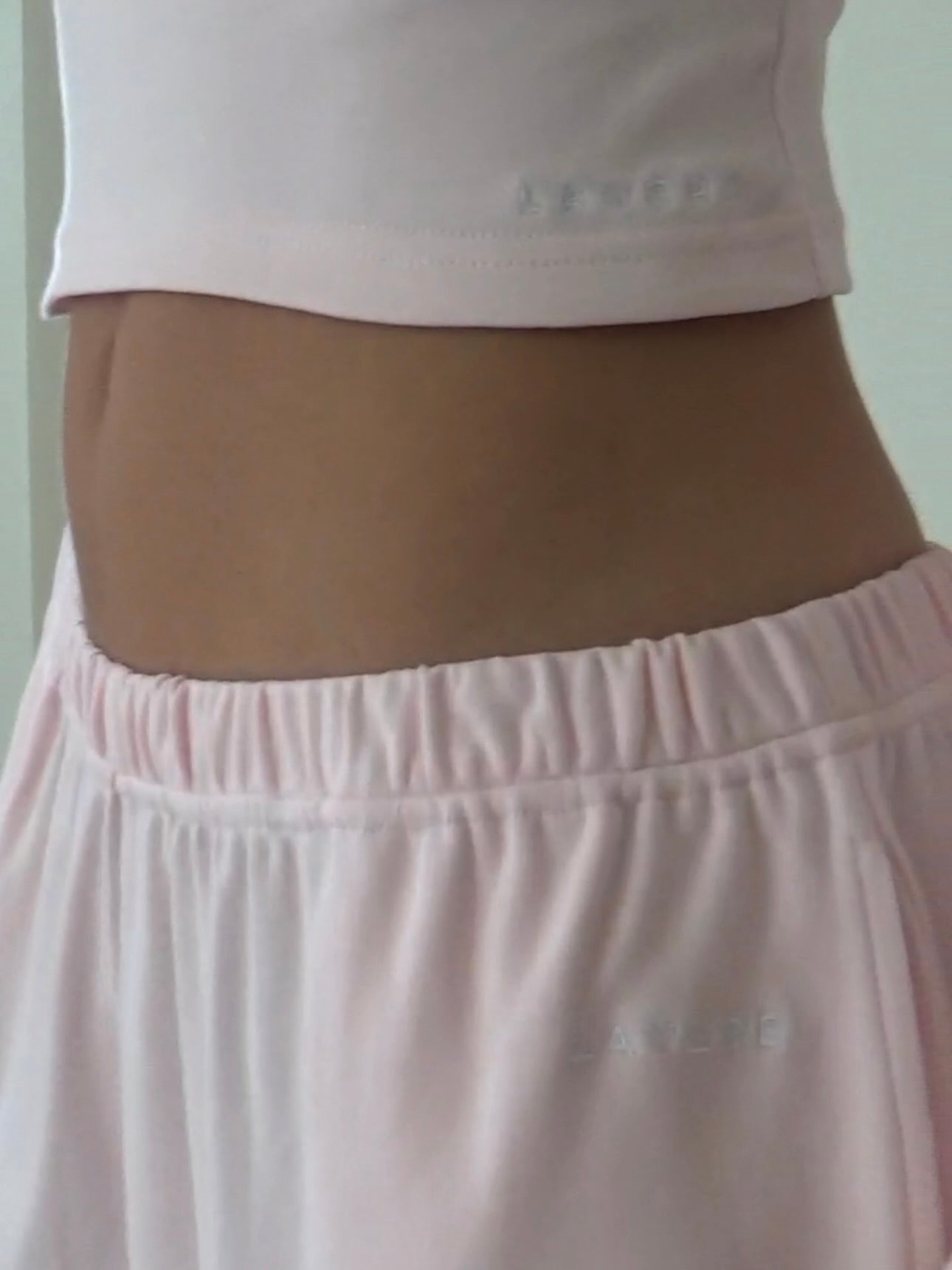 Woman wearing a light pink organic cotton long-sleeve top and organic cotton wide-leg pants against a white background