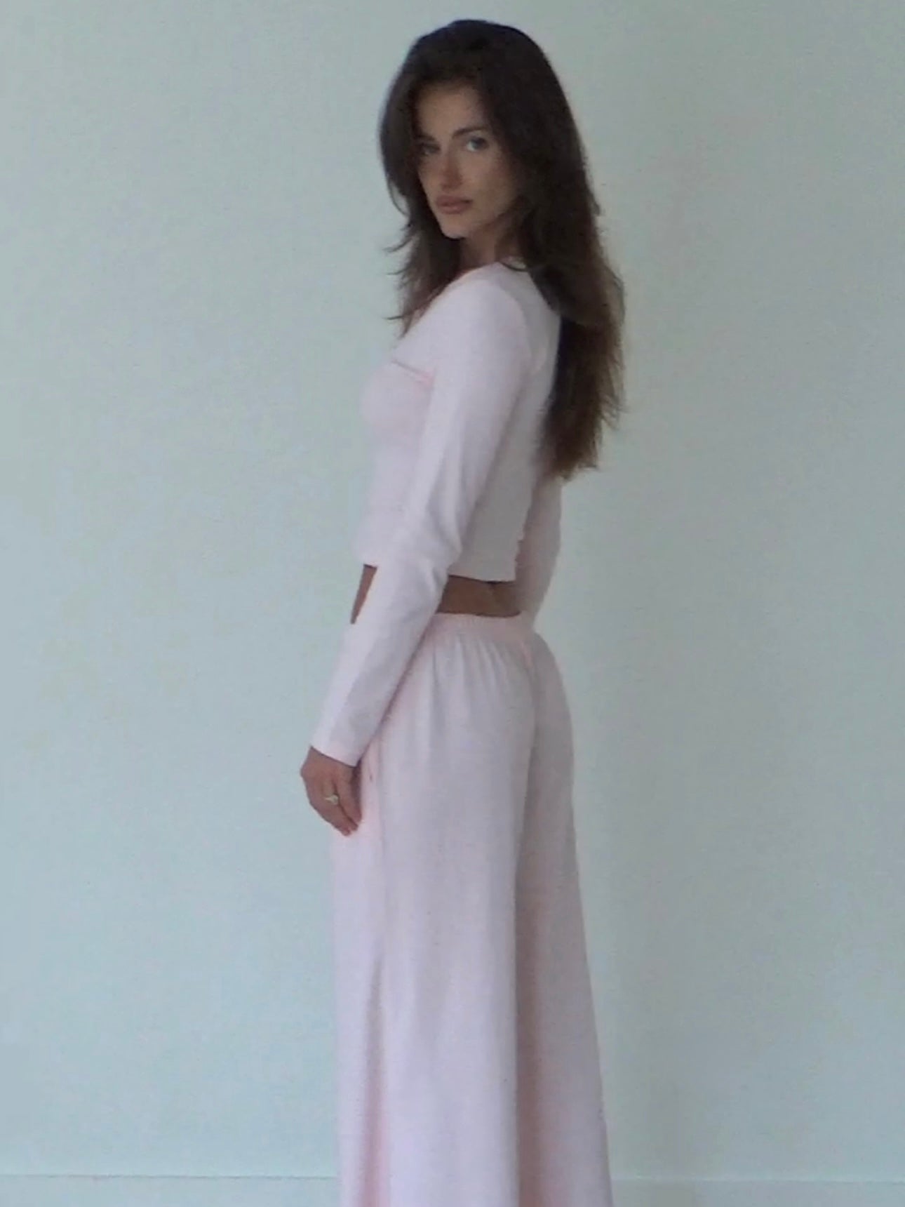 Woman wearing a light pink organic cotton long-sleeve top and organic cotton wide-leg pants against a white background